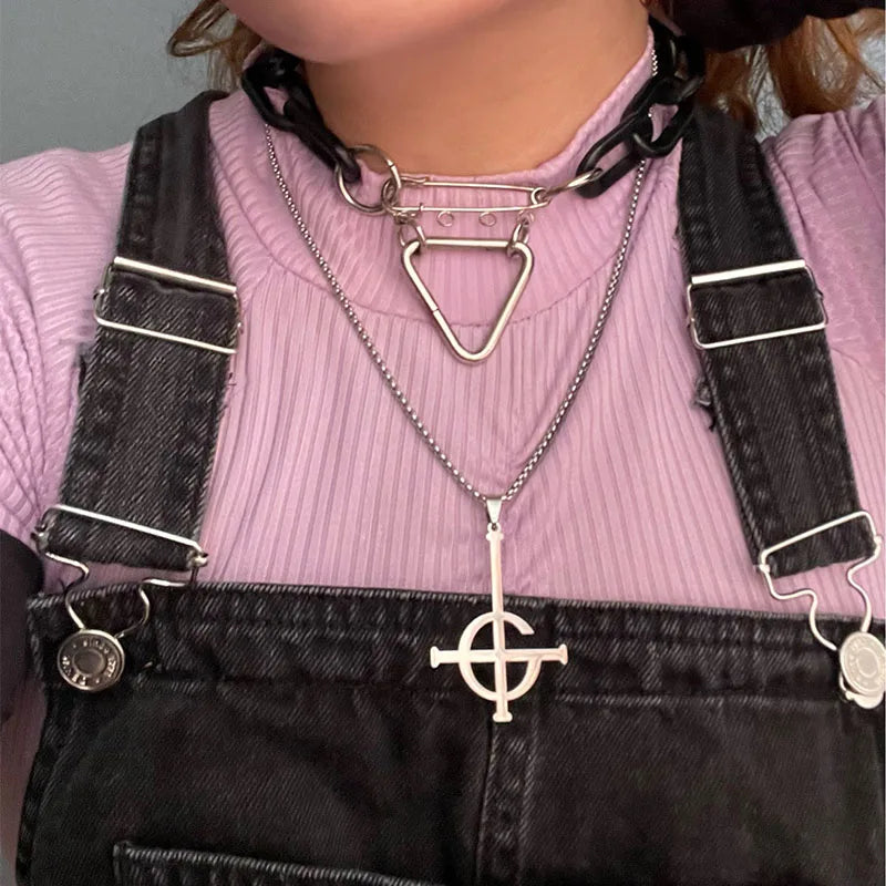 Person wearing a pink sweater and black overalls with necklaces featuring geometric pendants.