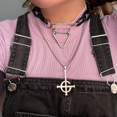 Person wearing a pink sweater and black overalls with necklaces featuring geometric pendants.