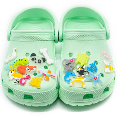 Green children's clogs with animal-themed shoe charms on a white background