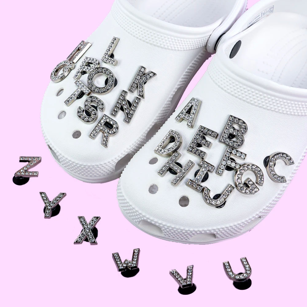 White clogs with shoe charms rhinestone letter charms on a pink background