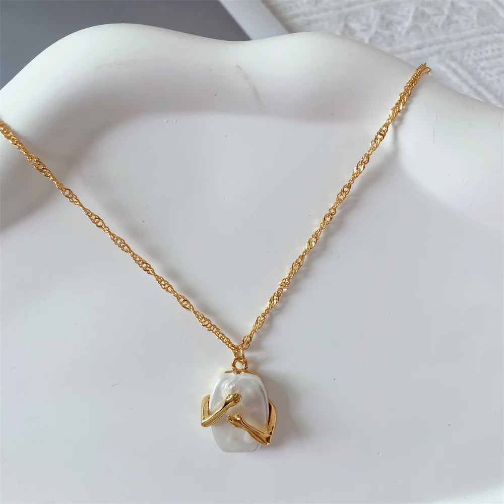 Gold necklace with a hands hugging a white Natural iridescent stone pendant on a white Dish