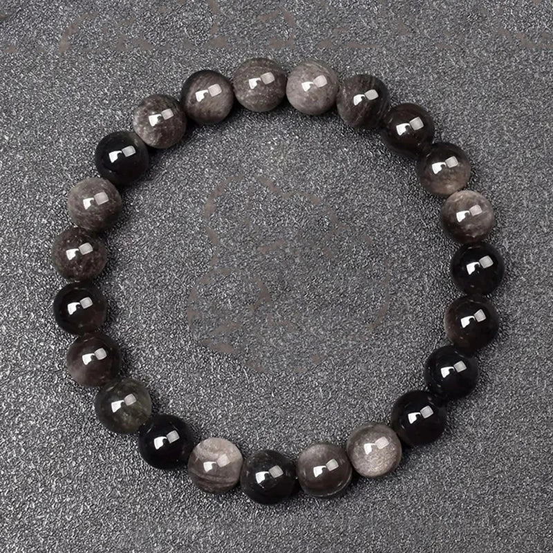 Round beaded bracelet with alternating dark and light beads on a gray surface