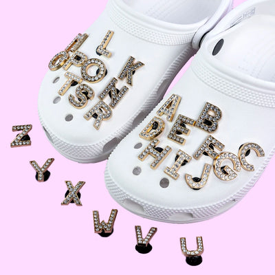 White crocs with rhinestone shoe charms letter charms on a pink background