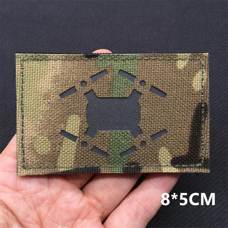 Camouflage patch with a mine black symbol held by a hand on a dark background