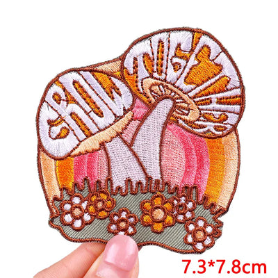 Embroidered patch with a mushroom design held by a hand, on a white background.