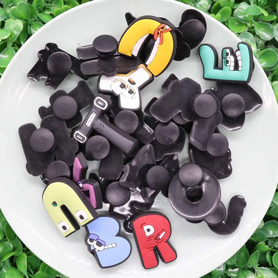 Assorted colorful letter-shaped shoe charms on a white plate with a green leafy background