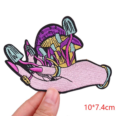 Embroidered patch of a hand holding mushrooms held by a hand, with dimensions 10*7.4cm.