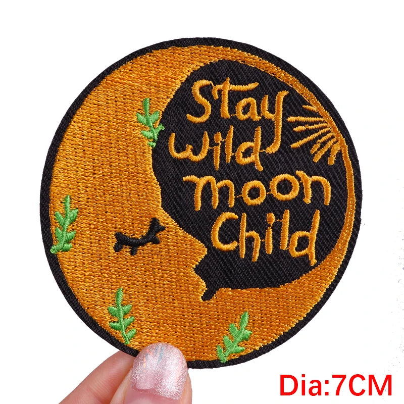 Circular patch with 'Stay wild moon Child' text on a brown background, held by a hand.