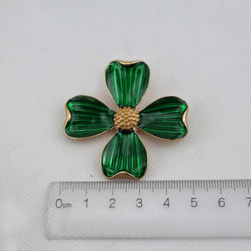 Green clover-shaped brooch with gold center on a white background with a ruler for scale.