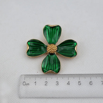 Green clover-shaped brooch with gold center on a white background with a ruler for scale.