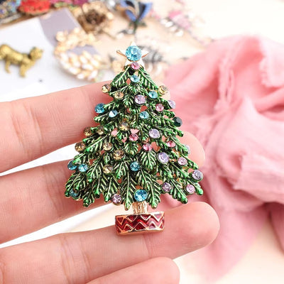 Decorative Christmas tree brooch with gemstones held in a hand against a blurred background.