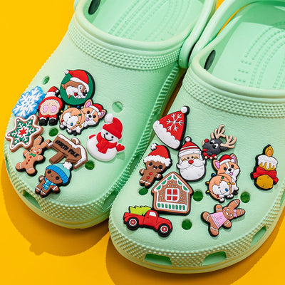 Light green clogs with Christmas-themed charms on a yellow background