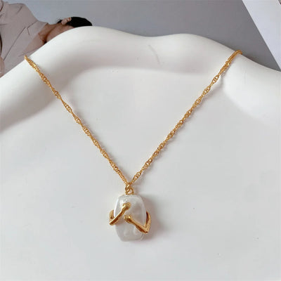 another view of a Gold necklace with pendant resembling hands hugging a white Natural iridescent stone pendant on a white Dish