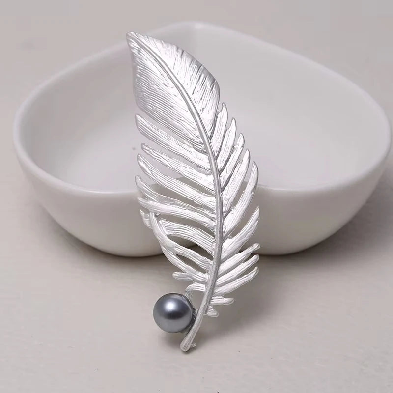 Silver feather-shaped brooch with a pearl on a light background