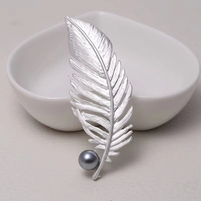 Silver feather-shaped brooch with a pearl on a light background