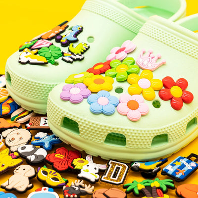 Green clog shoe with colorful decorative charms on a yellow background