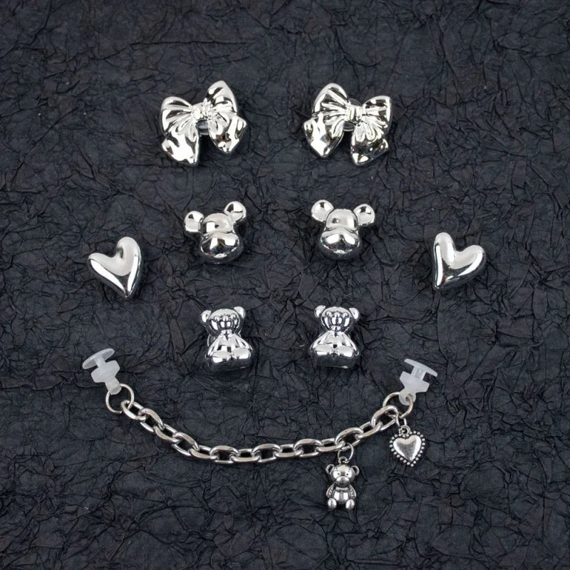 Collection of silver charms including bows, hearts, and teddy bears on a black textured background.