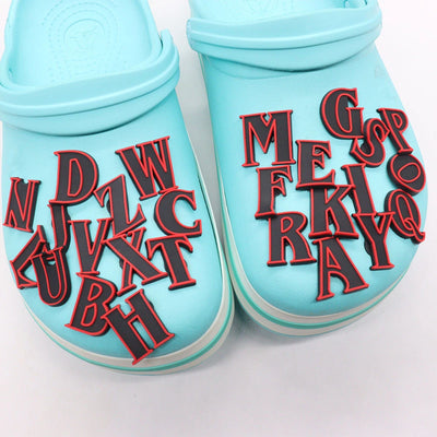 Pair of light blue slippers with red and black shoe charms letters on a white background