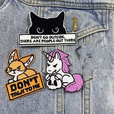 Three patches on a denim jacket: a black cat, a fox, and a unicorn with text.