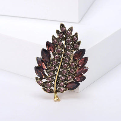 Decorative leaf brooch with purple gemstones on a white background
