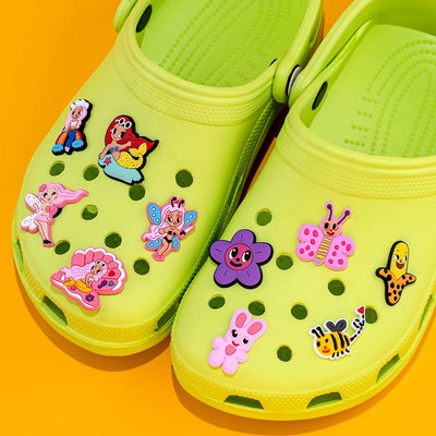 Green clogs with colorful character shoe charms on a bright orange background