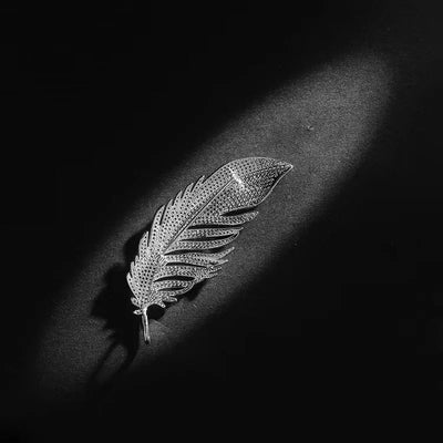 Silver feather-shaped brooch on a dark surface