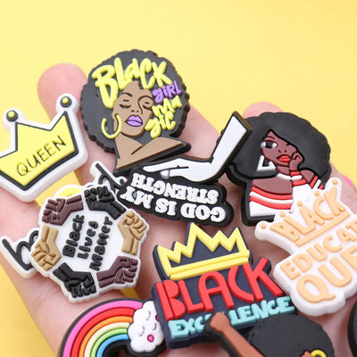 Collection of colorful 'Black Girl Magic' themed charms held in a hand against a yellow background.