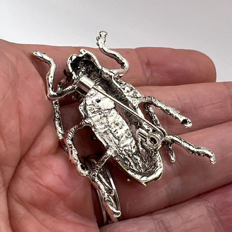 back side of a Decorative Red beetle-shaped brooch  held in a hand against a neutral background