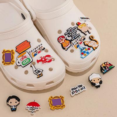 White clogs with colorful 'Friends' themed shoe charms on a beige background