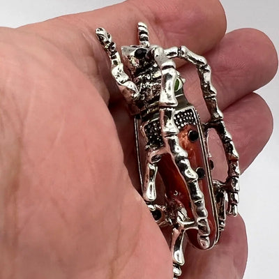 Side view of Decorative Red beetle-shaped brooch  held in a hand against a white background.