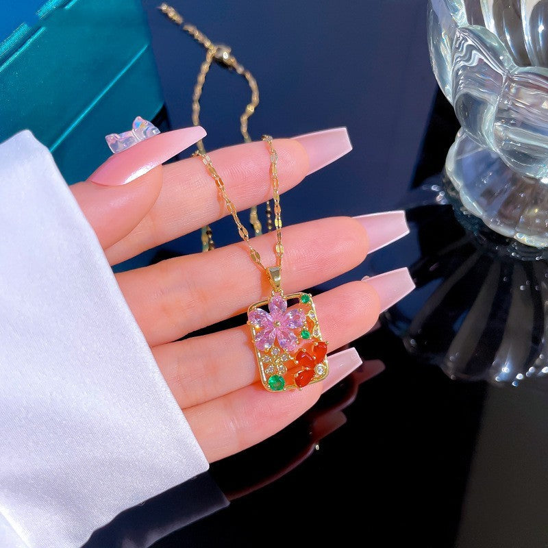 Colorful gemstone pendant on a gold chain held by a hand with pink nail polish.