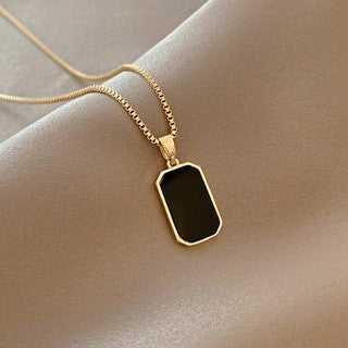 Gold necklace with a black pendant on a beige background