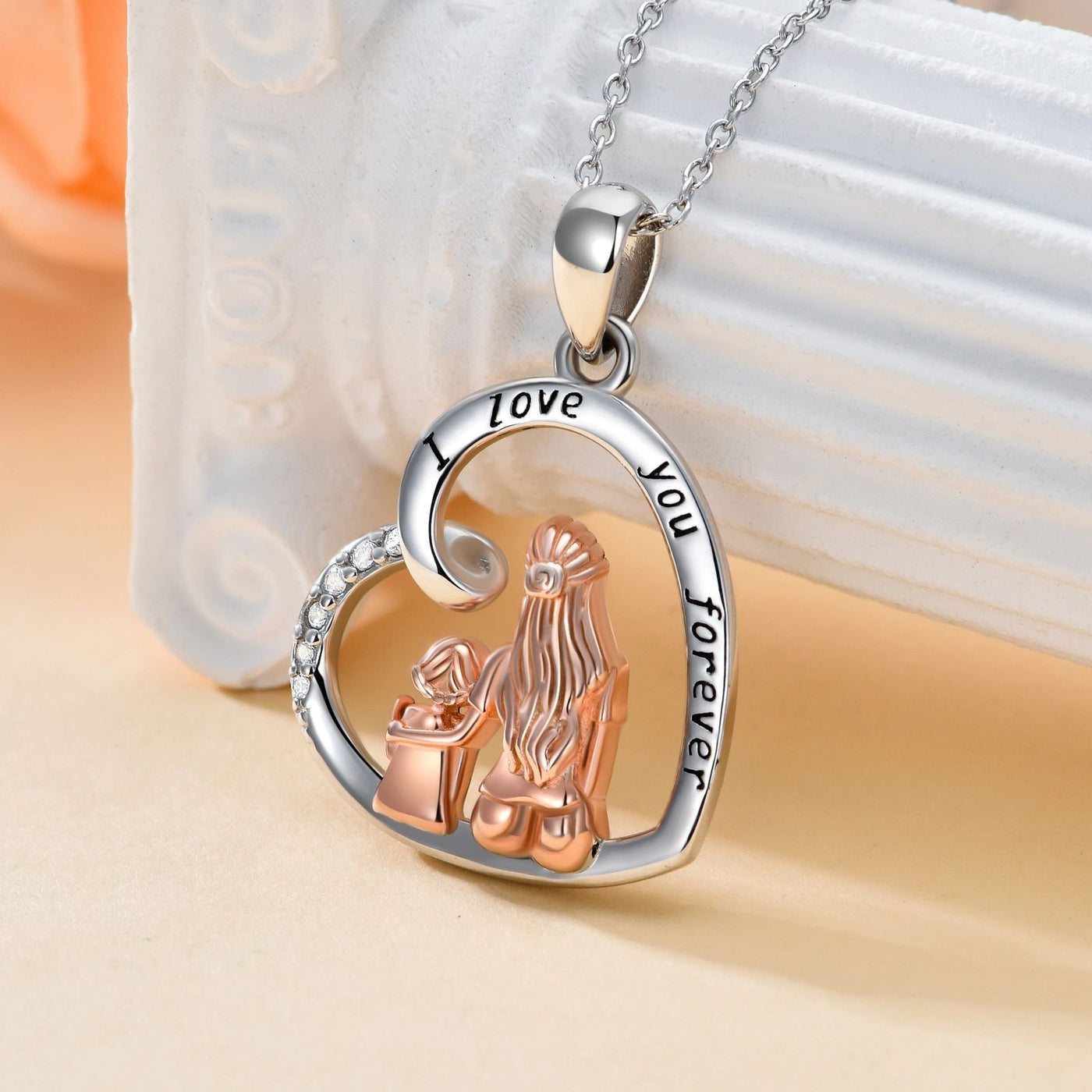 Heart-shaped pendant with two clasped hands and 'I love you forever' engraving on a beige background.