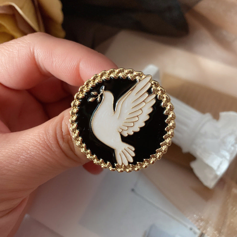 Hand holding a black and gold brooch with a white dove design.