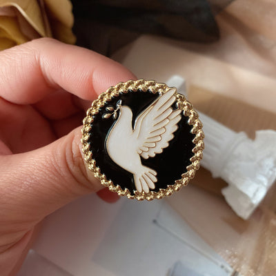 Hand holding a black and gold brooch with a white dove design.