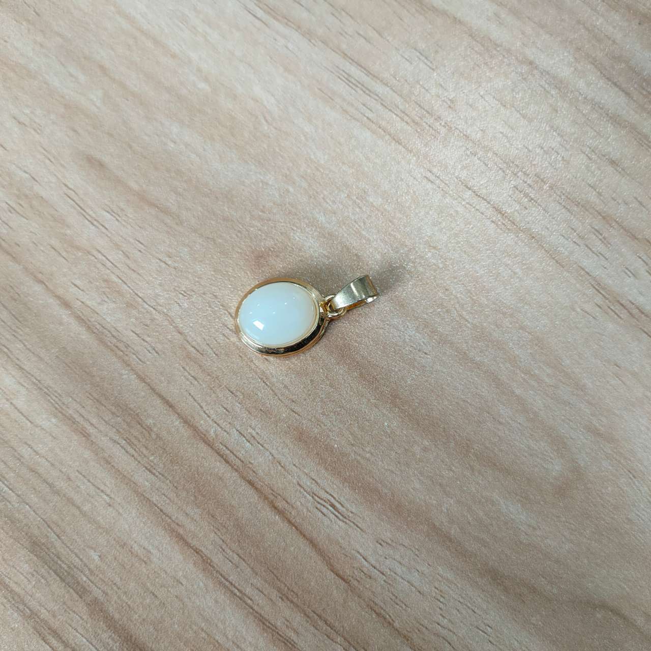 Gold pendant with a white stone on a wooden surface