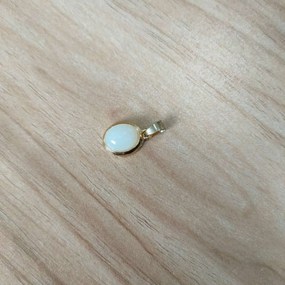 Gold pendant with a white stone on a wooden surface