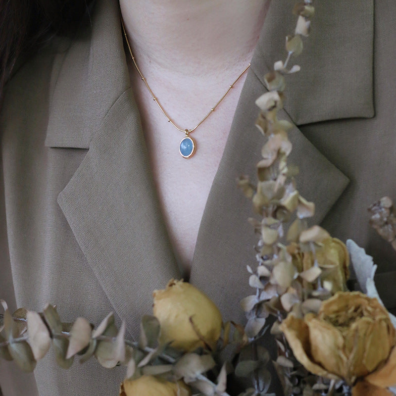 Necklace with a blue pendant worn by a person, surrounded by dried flowers and greenery.