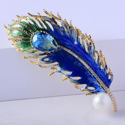 Decorative brooch with blue and green feathers on a white background