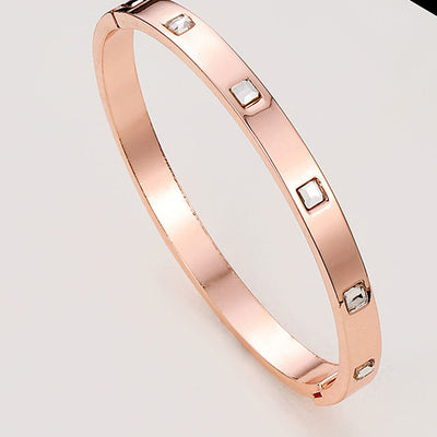 Rose gold bracelet with embedded stones on a light gray background