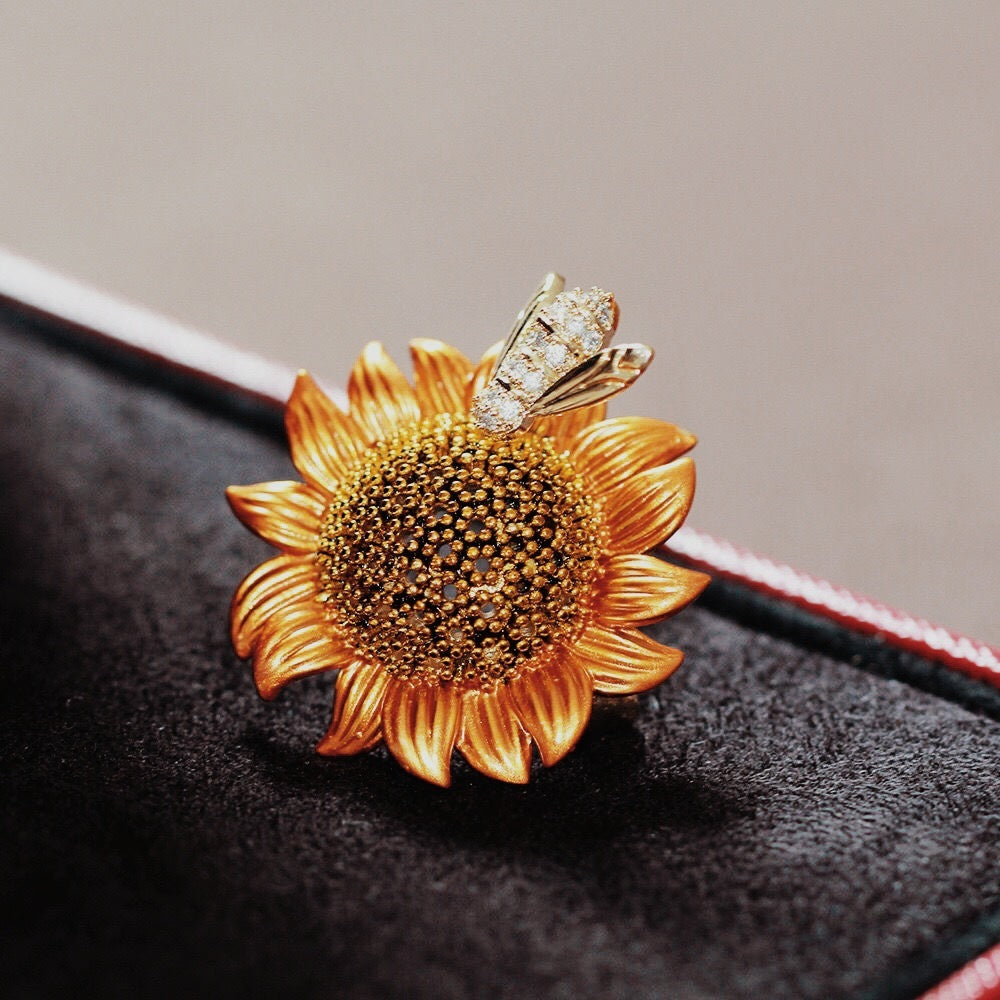 Gold sunflower-shaped brooch with a bee on a dark surface