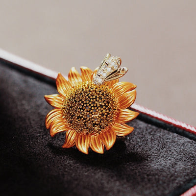 Gold sunflower-shaped brooch with a bee on a dark surface