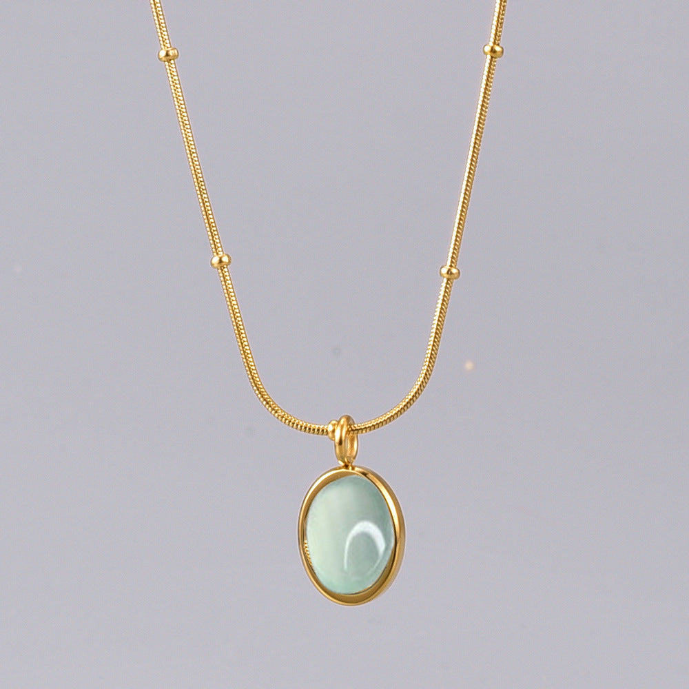 Gold necklace with a light green pendant on a gray background
