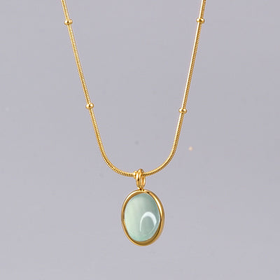 Gold necklace with a light green pendant on a gray background