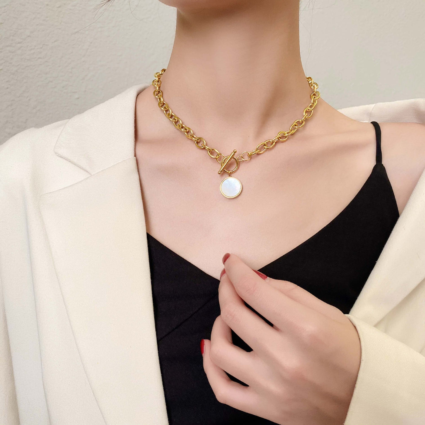 Person wearing a gold chain necklace with a round pendant on a neutral background