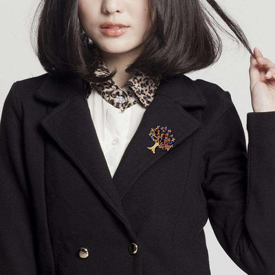 Person wearing a black coat with a colorful tree brooch, white shirt, and leopard print collar.