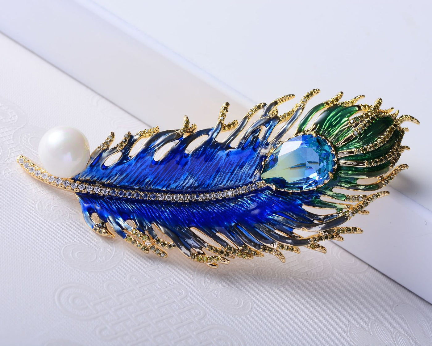 Decorative brooch with blue and green feathers and a pearl on a white background