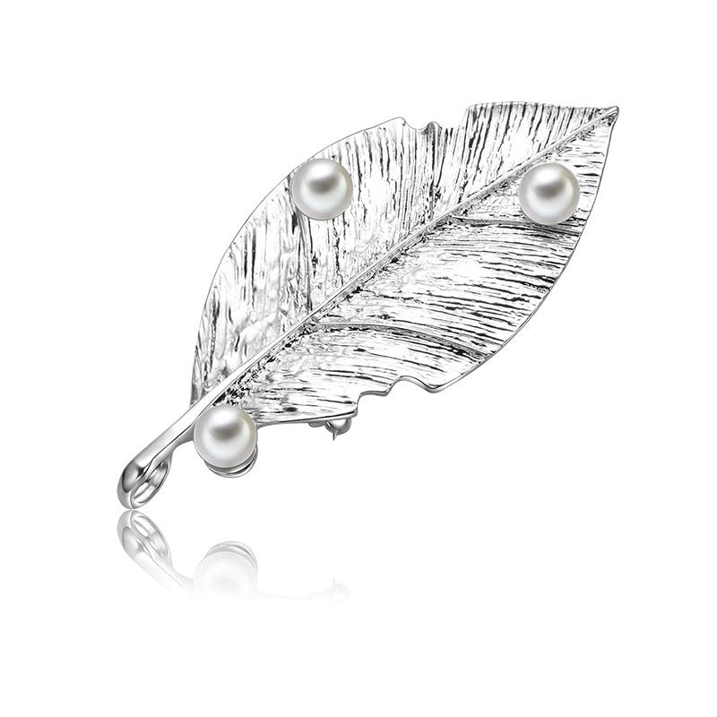 Silver leaf-shaped brooch with three pearls on a white background
