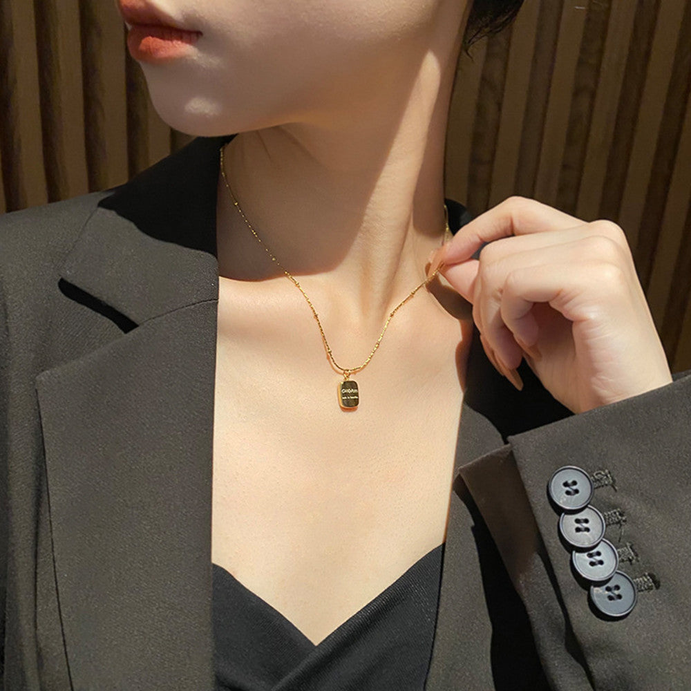 Person wearing a gold necklace with a pendant, adjusting it with their hand.