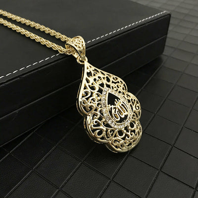 A gold pendant with a delicate filigree design and sparkling rhinestones rests on a black textured surface, evoking elegance and luxury.